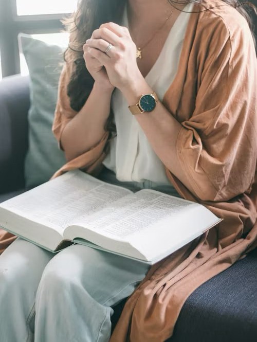 A woman's clasped hands resting on an open Bible in her lap